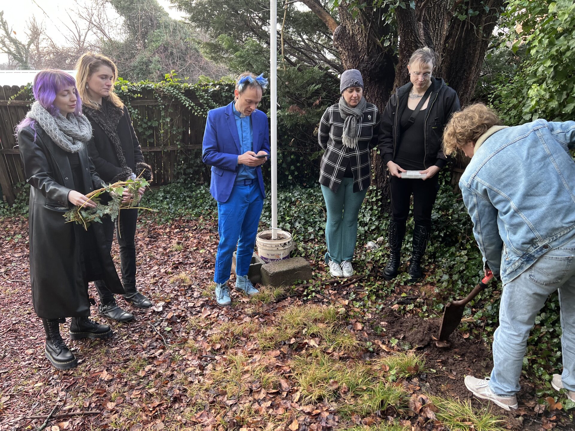 group of people outside watching one person cover a grave with earth